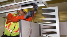 An electrician on a ladder rewiring a ceiling light fixture during a lighting retrofit.