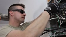 An electrician in work gloves connecting wiring inside an open electrical enclosure.