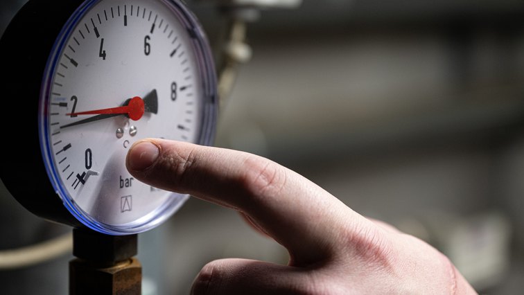 A technician's hand checking a round pressure gauge on heating equipment during a maintenance visit.