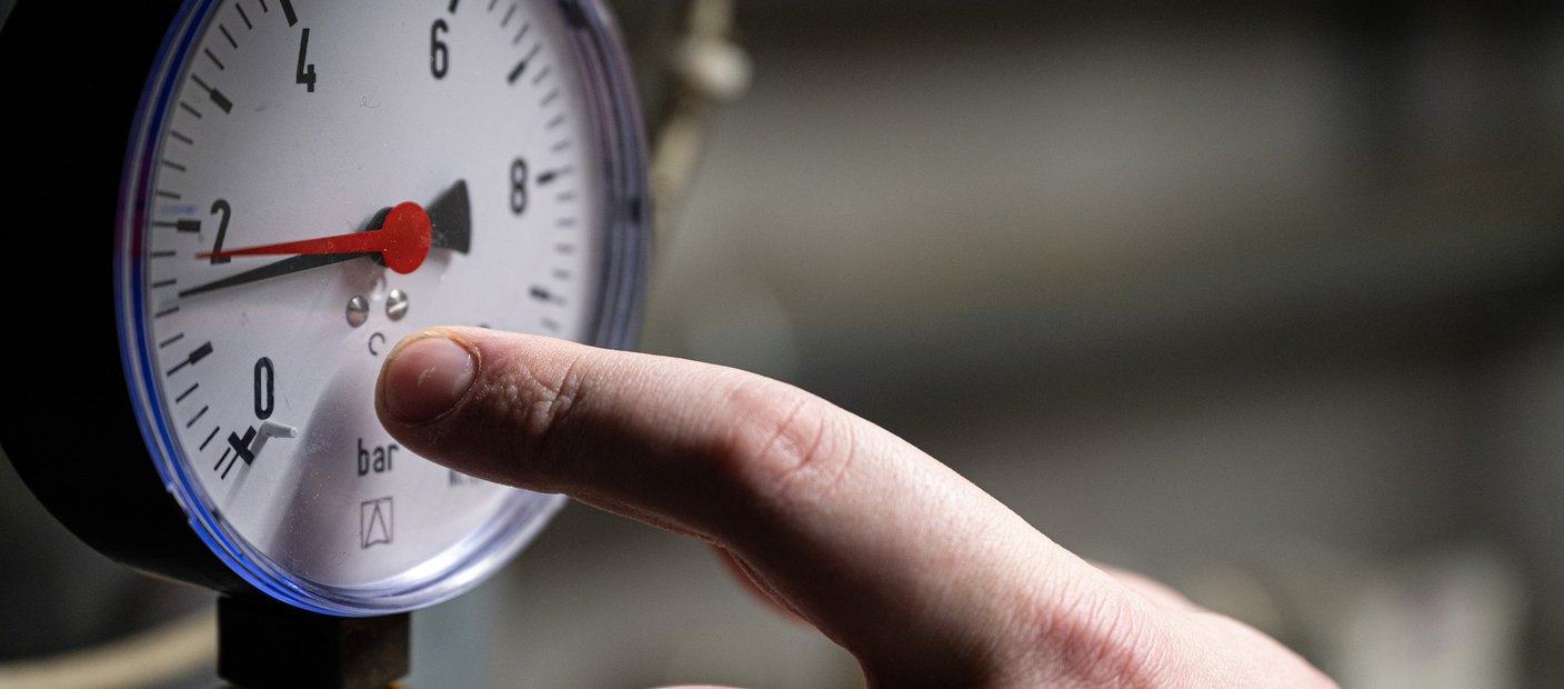 A technician's hand checking a round pressure gauge on heating equipment during a maintenance visit.