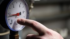 A technician's hand checking a round pressure gauge on heating equipment during a maintenance visit.