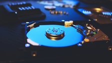 The inside of an opened computer hard drive, showing the platter and the read head arm.
