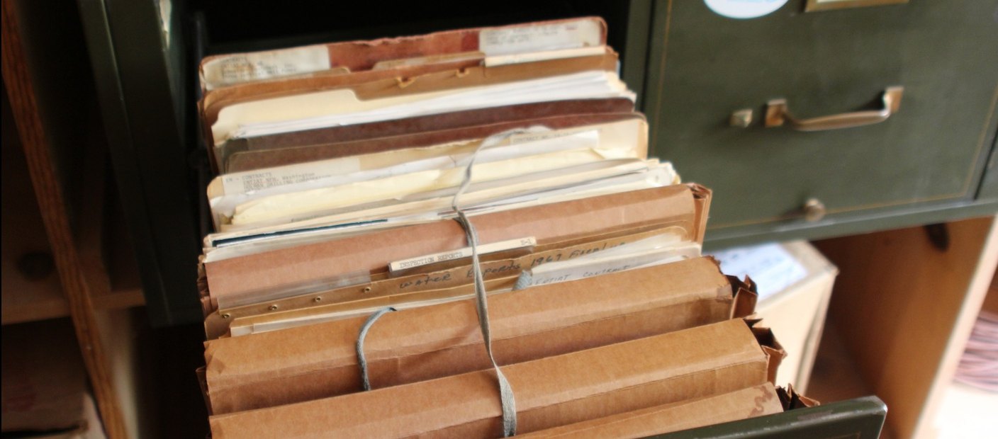 Bundles of old paper files tied with string inside the drawer of a metal filing cabinet.