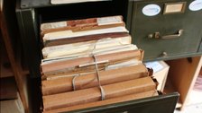 Bundles of old paper files tied with string inside the drawer of a metal filing cabinet.