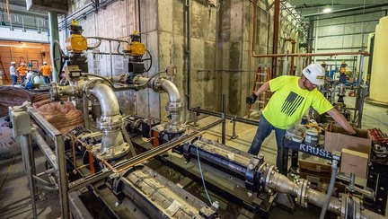 A plumber in a hard hat and high-visibility vest working on large industrial pipework.