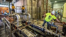 A plumber in a hard hat and high-visibility vest working on large industrial pipework.