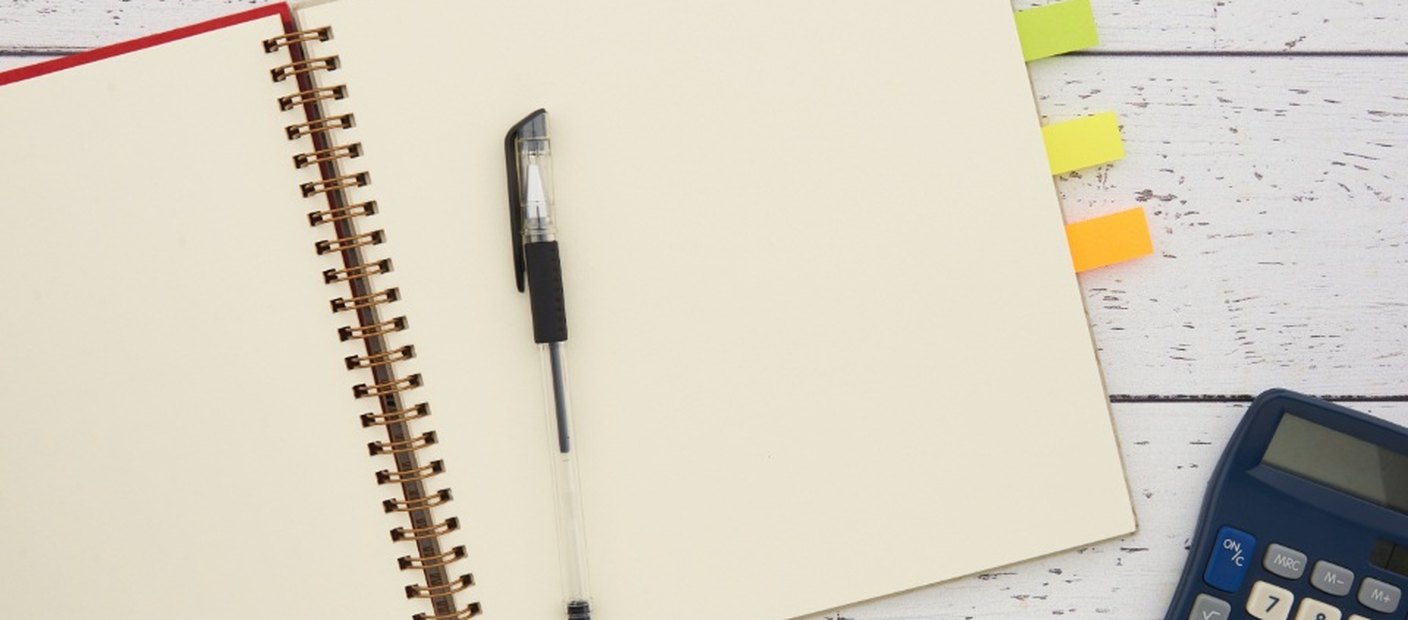 An open ruled notebook with a pen, coloured index tabs and a calculator on a white desk.