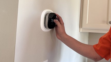 A technician's hand setting a round wall thermostat inside a customer's home.