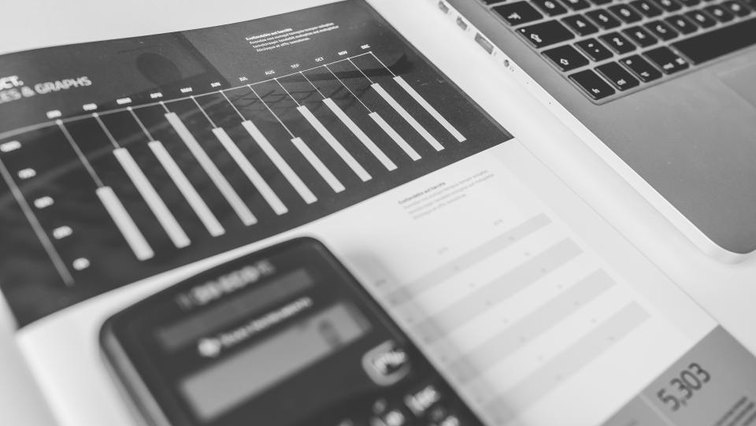 A pocket calculator resting on printed bar charts beside a laptop, in black and white.