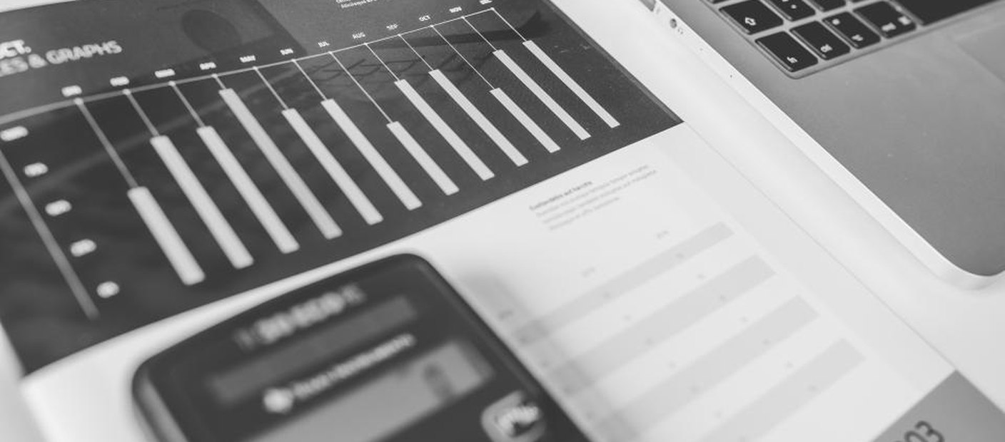 A pocket calculator resting on printed bar charts beside a laptop, in black and white.